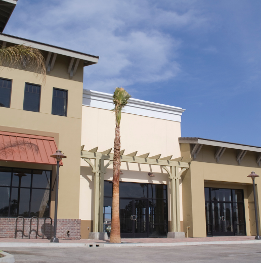 Exterior of a beige commercial building with a palm tree in front and a clear blue sky above.