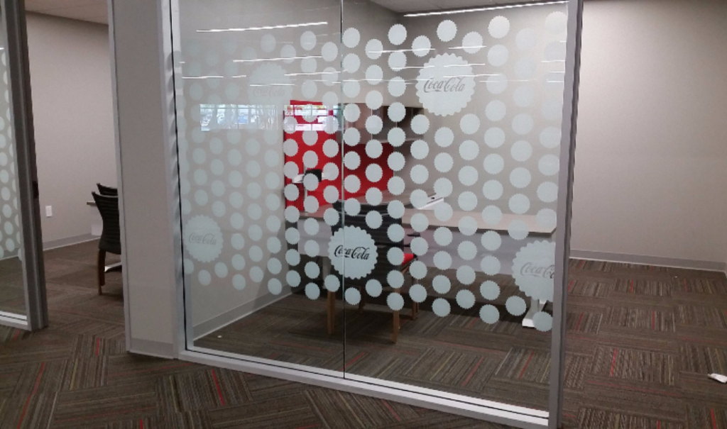 Glass office partition with frosted Coca-Cola logo and dot pattern design.