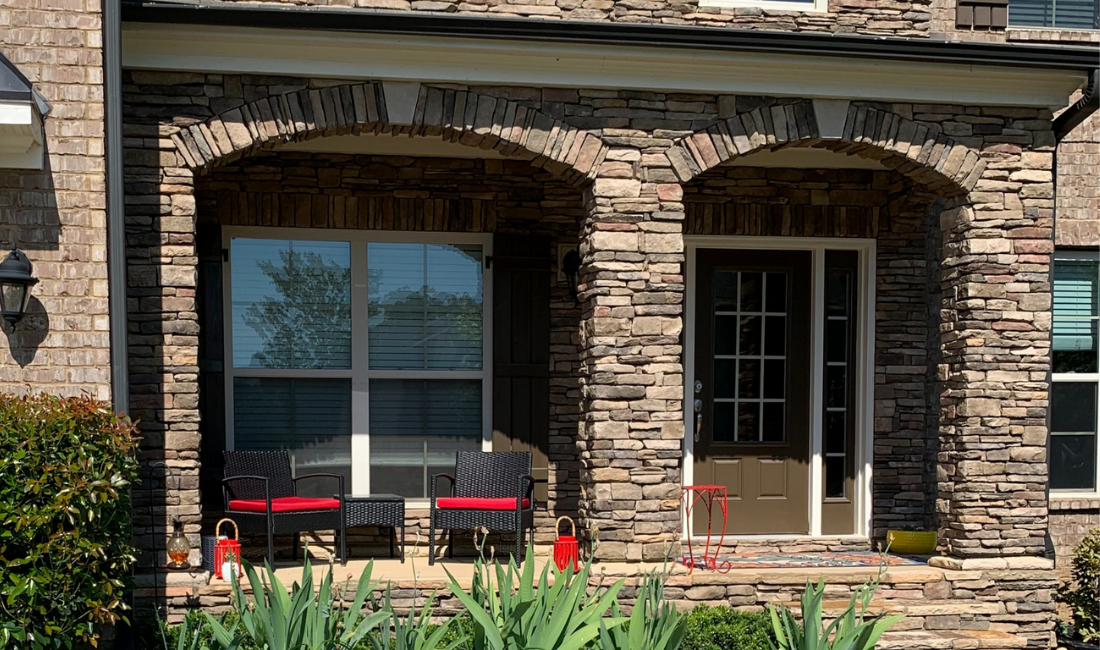 Front view of a house with stone archways, a glass door, and outdoor seating with red cushions.