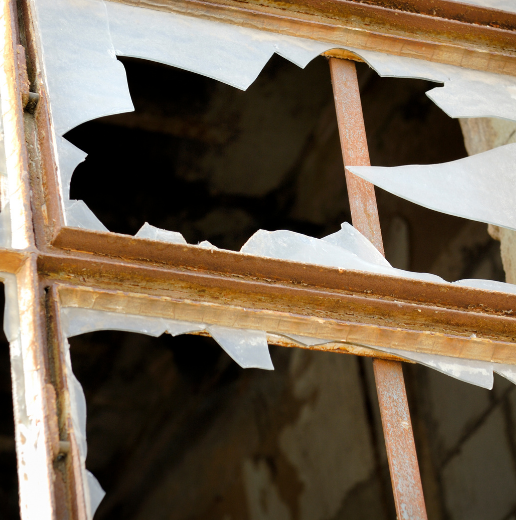 Close-up of a broken window with shattered glass and rusty frame.
