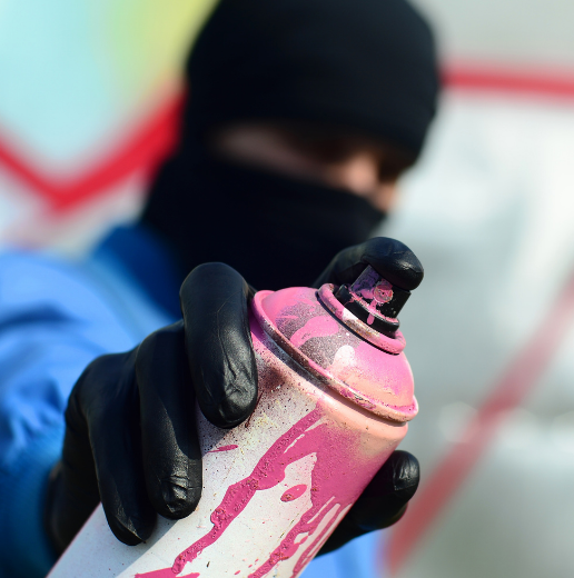 Close-up of a person's hand in a black glove holding a pink spray paint can, with a blurred background.