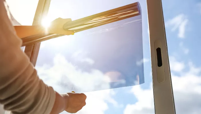 A person applying a tint film to a window, with sunlight shining through.