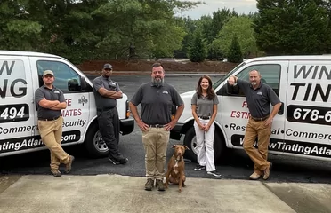 A team of five window tinting professionals and a dog standing confidently in front of their service vans.